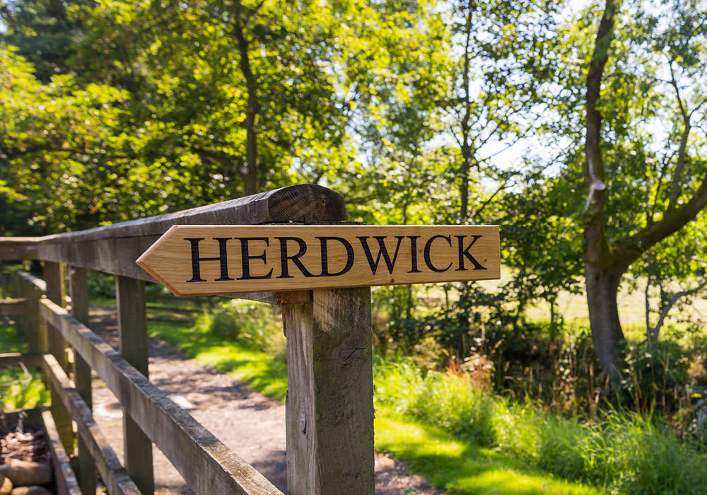 a wooden sign srewed to a fence post with the name Herdwick stamped on it in large black letters