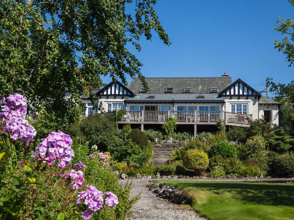 The Old Pavilion, a large white house with wooden balcony overlooks the beautiful mature gardens at Settledown Retreats