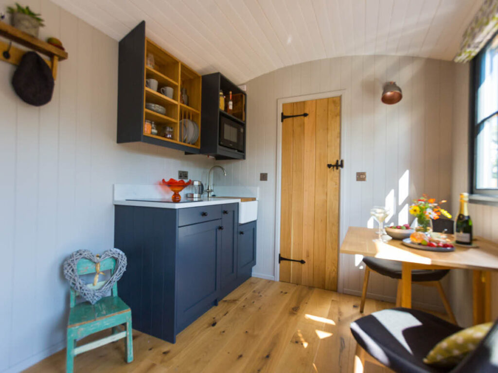 a wide angle shot of the inside of a Settledown Retreat shepherd hut, nicely equipped with a compact fitted kitchen and dining area for two