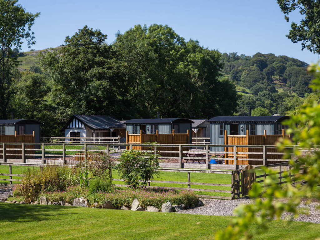 a shot from distance viewing the shepherd huts at Settledown Retreats and the tree covered fell in the background