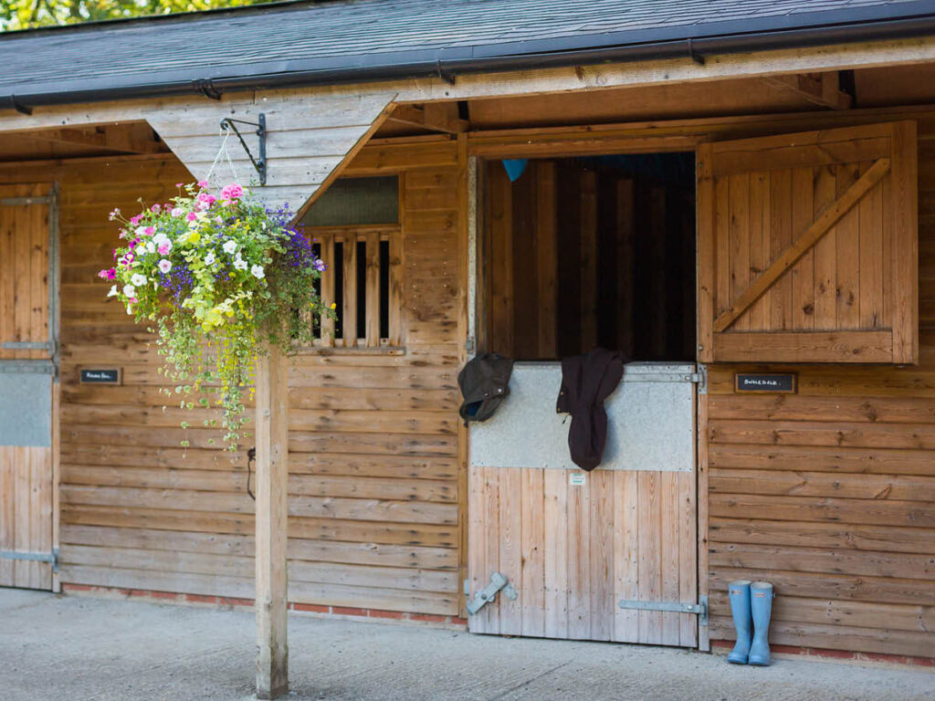 a shot of the stables with a hanging basket full of blossoming wild flowers at Settledown Retreats. The top half of the door swung open and a coat hung over the bottom half