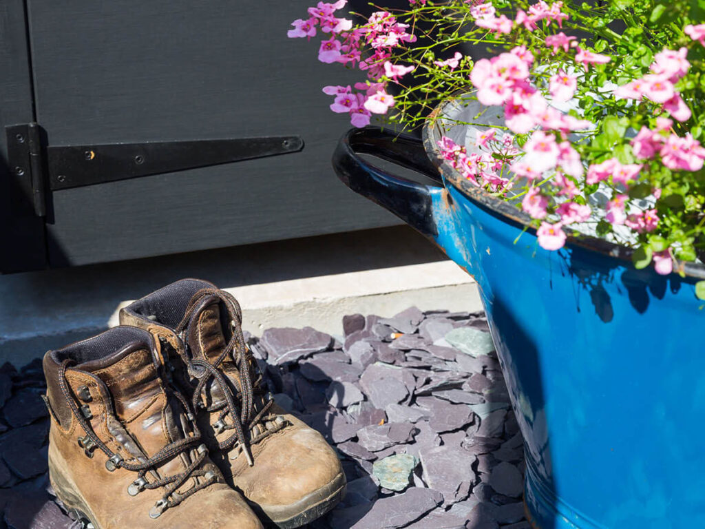 brown leather walking boots sit on blue slate chippings, lovely pink flowers in the foreground
