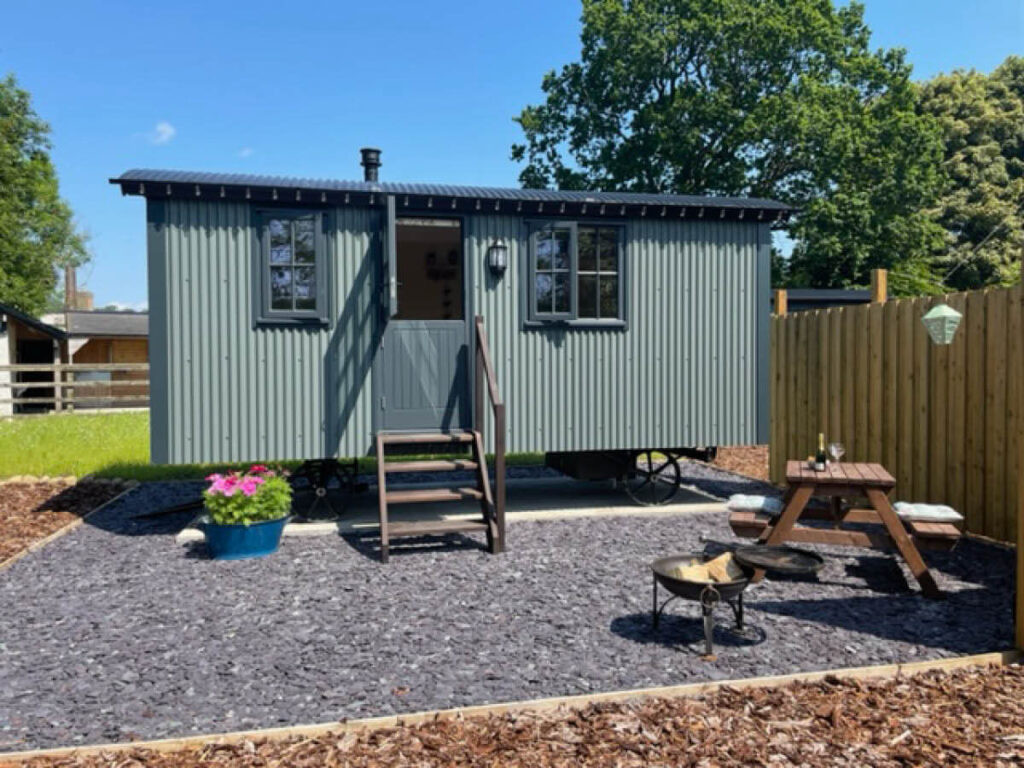 the private patio area outside one of the Settledown Retreats shepherd huts, with a colourful flower basket, fire pit and patio table