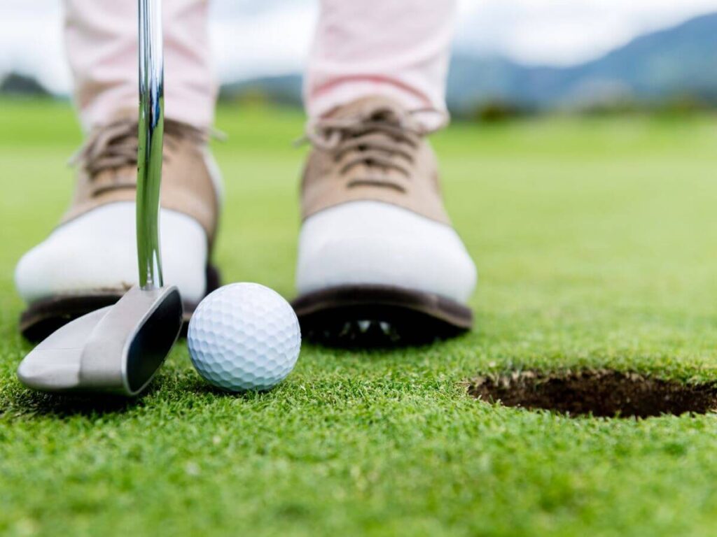 a close up shot of a golfers clean white shoes taken as they line up a put just a few inches from the hole on a golf green