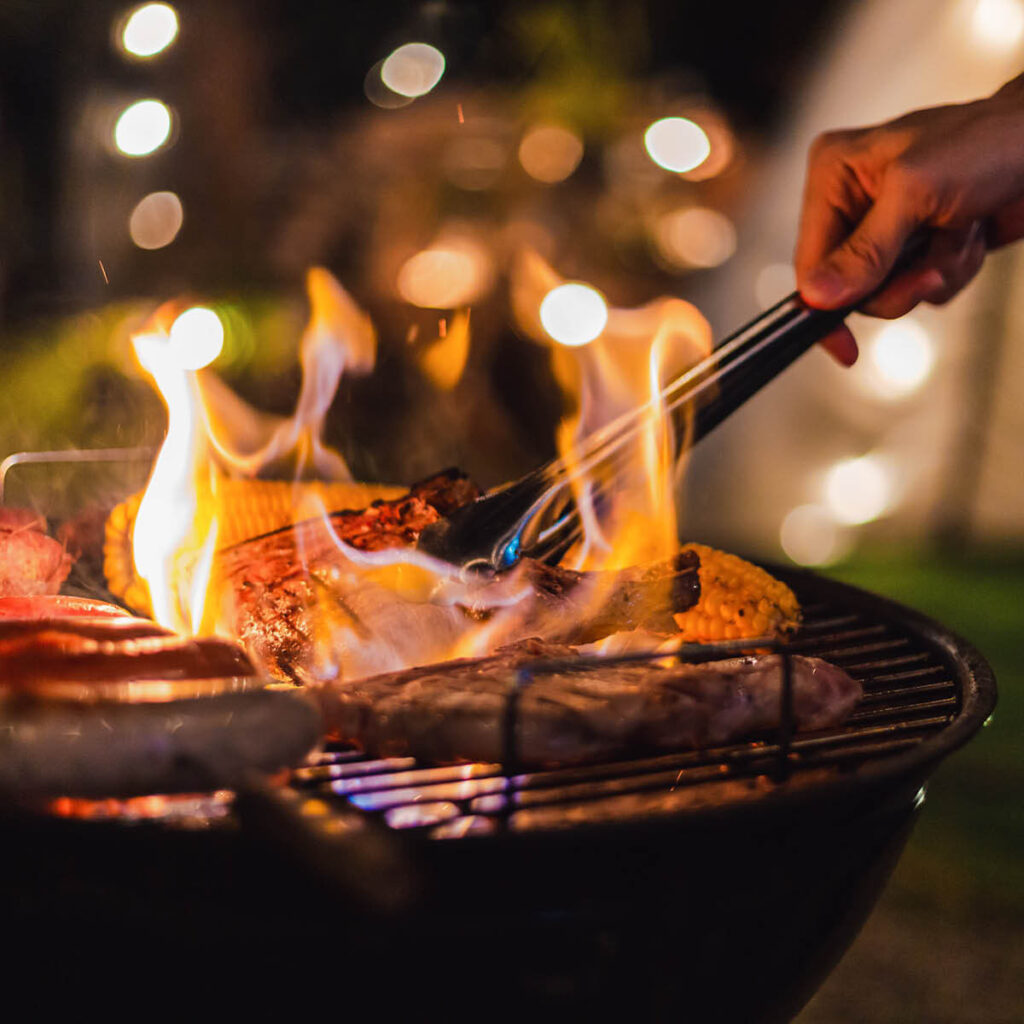 a night time shot od flames rising from a bbq while someone turns over the food