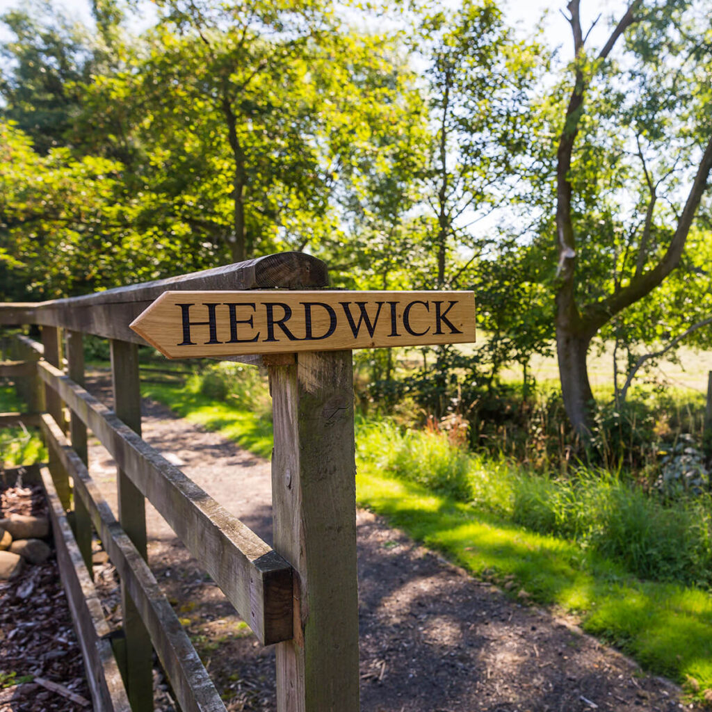 a wooden sign srewed to a fence post with the name Herdwick stamped on it in large black letters
