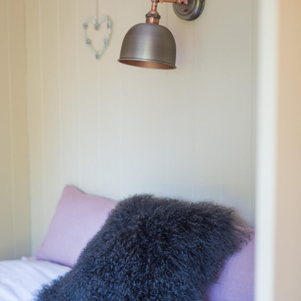 a close up shot of pillows and cushions decorating a bed, a decorative lamp and heart shape on the wall above