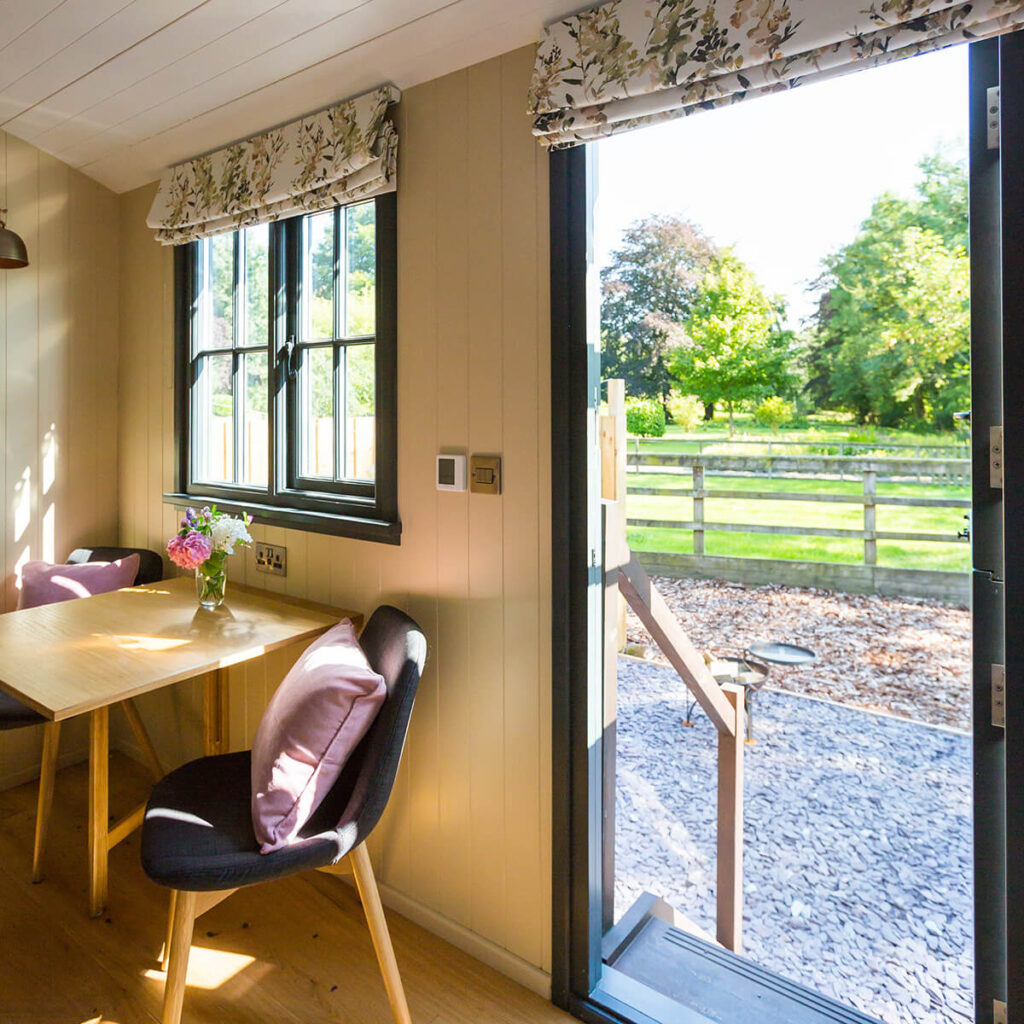 looking the open door of a shepherd hut from the inside, a private patio area with mature trees in the background