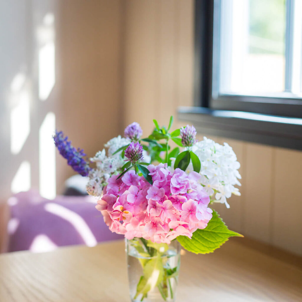 a vase of wildflowers sitting on a dining table with sun streaming in through the window