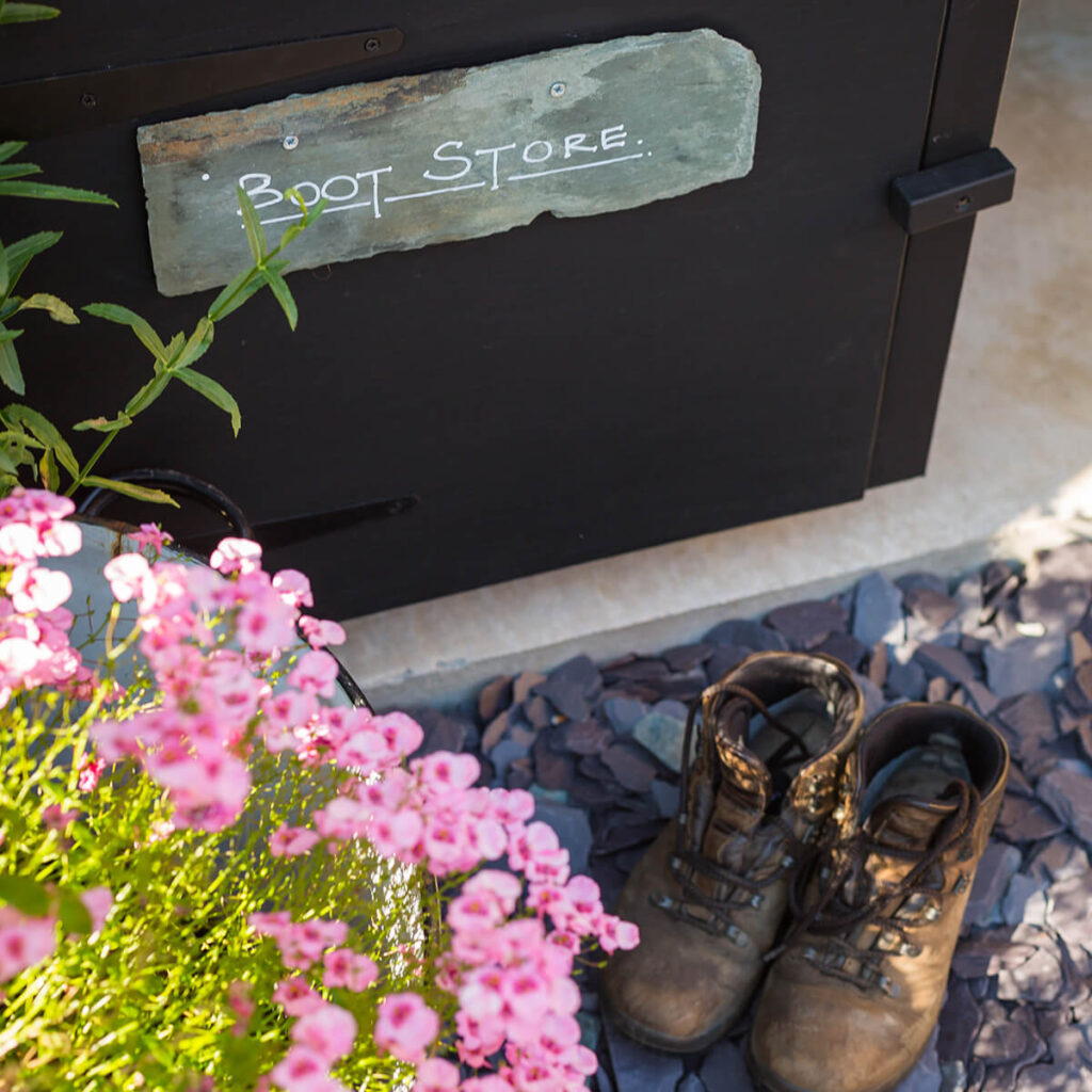 brown leather walking boots sit on blue slate chippings, lovely pink flowers in the foreground