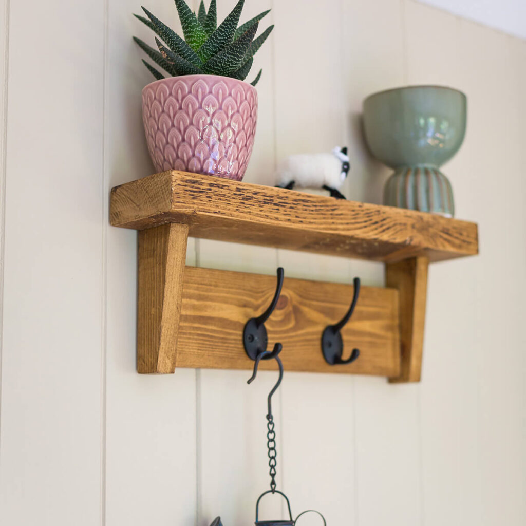 a small wooden shelf with a plantpot and ornaments on top, and two coat hooks on the front