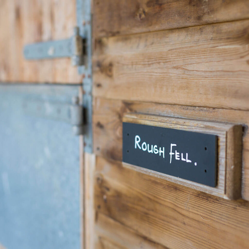a black slate sign srewed to a stable with the name of Rough Fell written on it in white marker