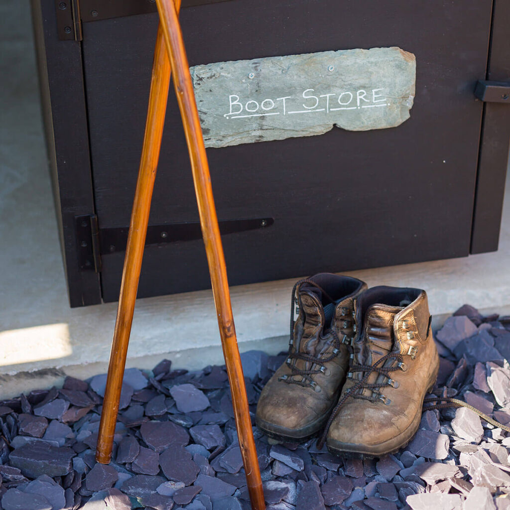 walking boots and a pair of walking sticks sit on blue slate chippings aside a lockable boot store