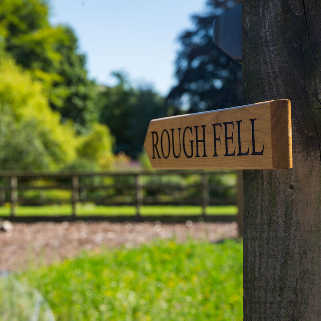 a wooden sign points the way to the Rough Fell shepherd hut at Settledown Retreats