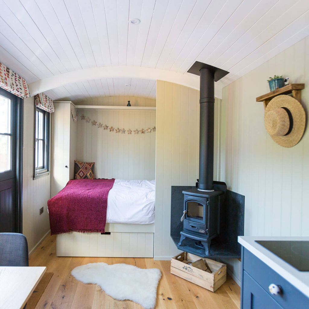 a view of the king size bed and wood burning stove inside one of the beautifully fitted out shepherd huts at Settledown retreats
