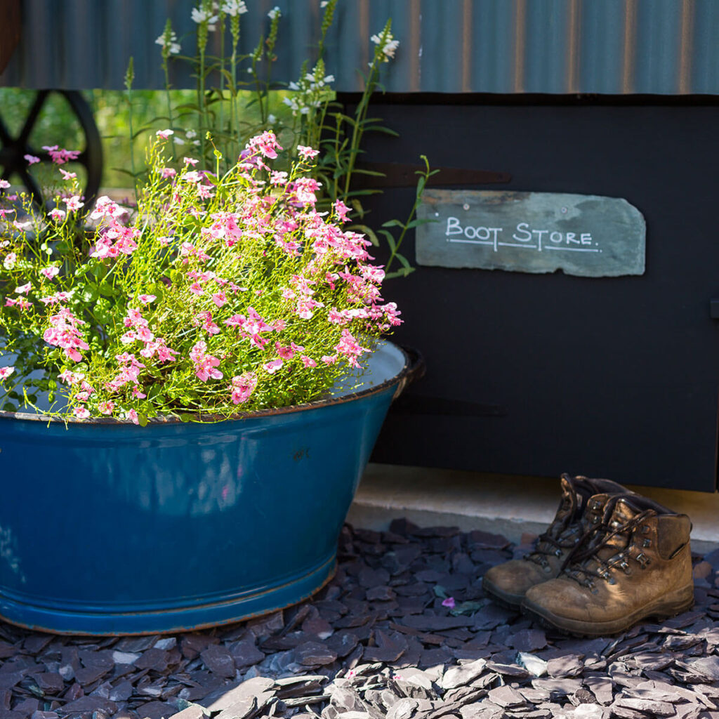 a pair of walking boots sitting beside a rustic enamel pot filled with wild flowers