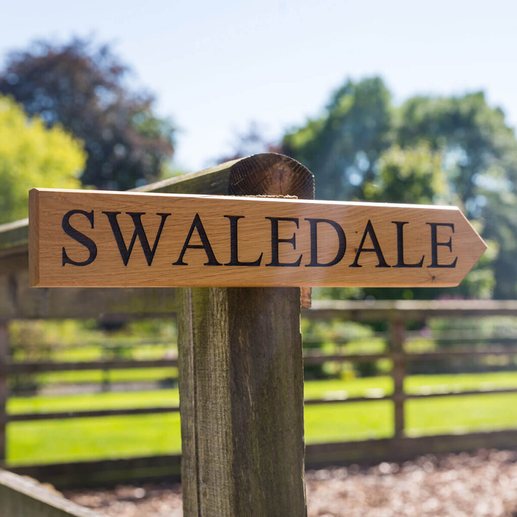 a wooden sign post points the way to the Swaledale shepherd hut at Settledown Retreats